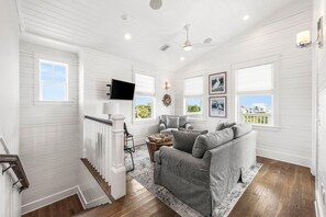 A spacious living room with a large gray sectional sofa, a flat-screen TV mounted on the wall, and a staircase leading to an upper level. - Serenity by the Sea 30A (Panama City Beach)