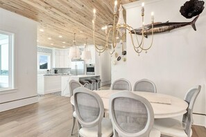 A modern dining area with a round table and six chairs, a wooden ceiling, and a chandelier. - Amberjack (Panama City Beach)