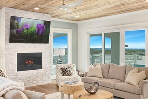 A modern living room with a fireplace, a flat-screen TV, and a large window offering a view of the ocean. - Amberjack (Panama City Beach)