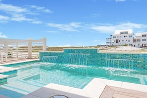 A swimming pool with a waterfall feature, surrounded by a white fence and a building with multiple balconies. - Amberjack (Panama City Beach)