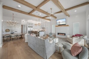 A spacious living area with a fireplace, a television mounted above it, and a dining area with a modern kitchen in the background. - Coral Cay (Panama City Beach)