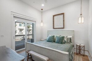A bedroom with a bed, bedside tables, a bench, a framed picture on the wall, and a view through a sliding door. - Coral Cay (Panama City Beach)