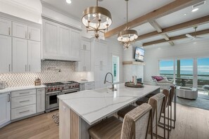 A modern kitchen with white cabinetry, a large island, and pendant lighting. - Coral Cay (Panama City Beach)