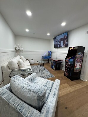 A room with a sofa, a small table, a television, and arcade machines. - Blue Fin (Panama City Beach)