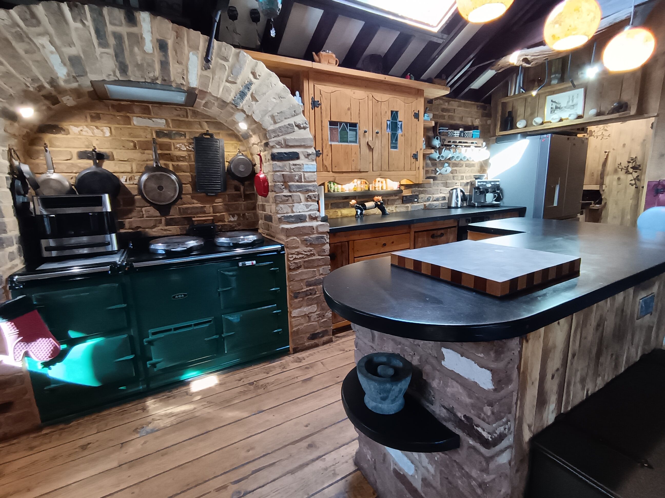 A rustic kitchen with a stone archway, wooden cabinets, and a central island with a black countertop.