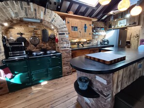 A rustic kitchen with a stone archway, wooden cabinets, and a central island with a black countertop.