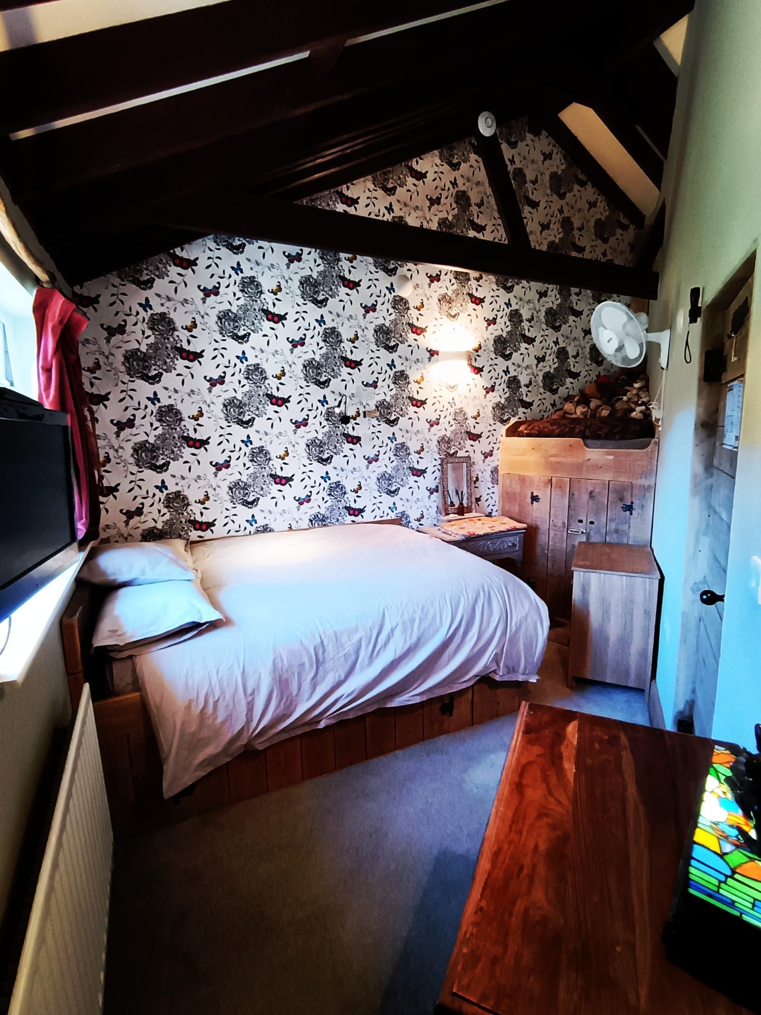 A bedroom with a bed, bedside table, dresser, and a window with curtains.