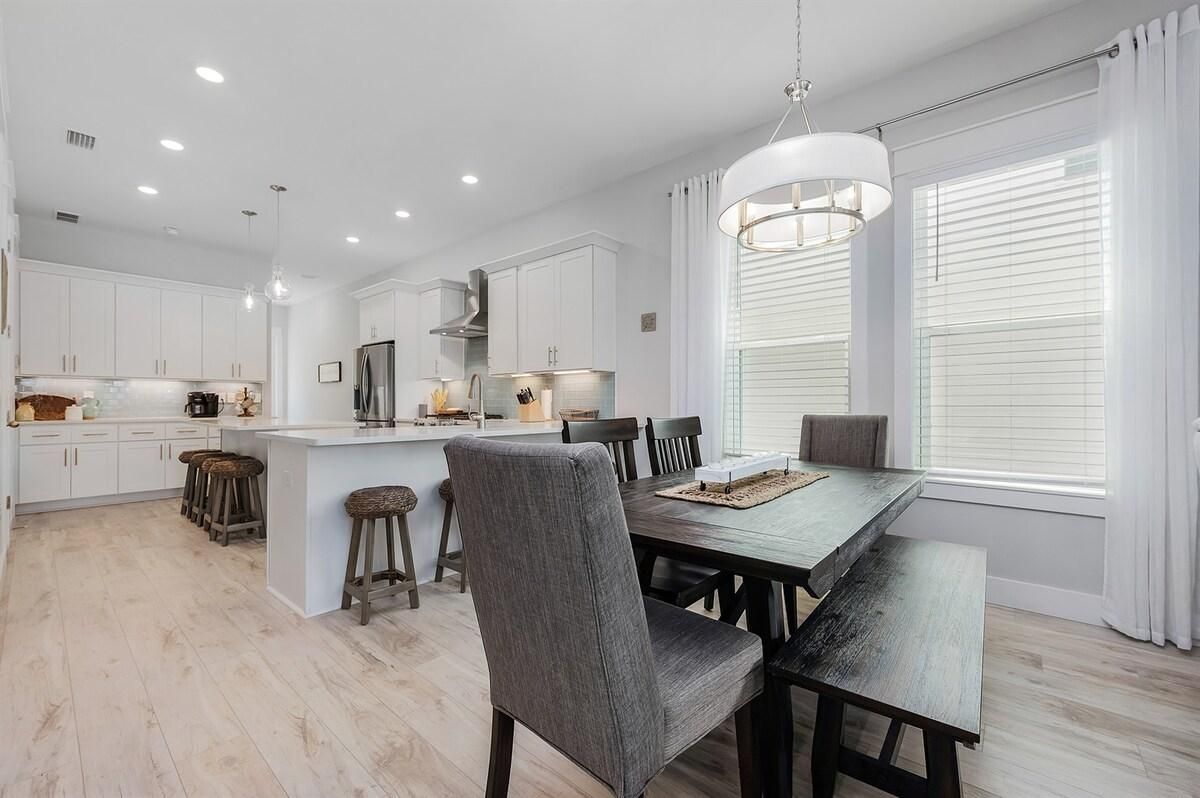 A modern kitchen with white cabinetry, a central island, and a dining area with a wooden table and chairs.