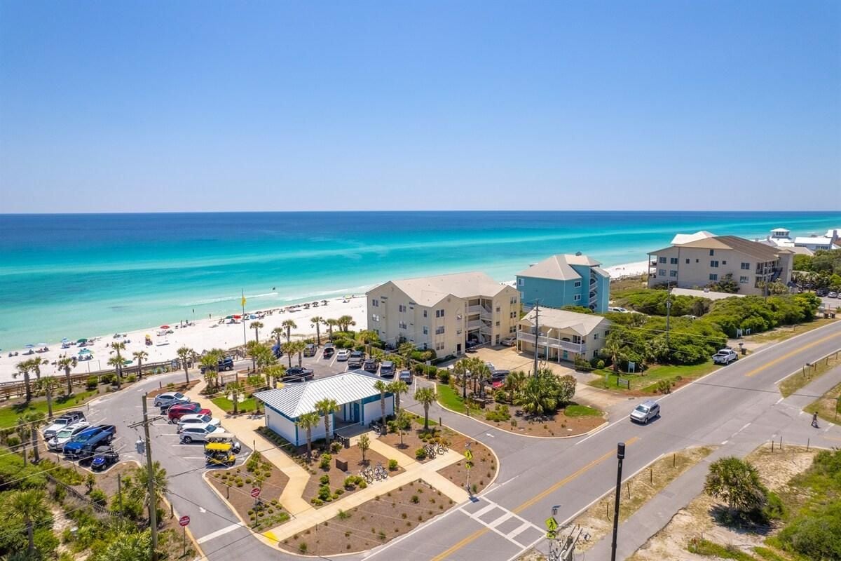 A coastal hotel with a parking lot, beach view, and a clear sky.