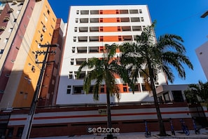 A multi-story building with a white facade and orange accents, featuring balconies and a palm tree in the foreground. - Apt. in Condo. nr. Beach Dgs0508 (Maceió)