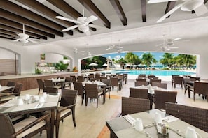 A restaurant with outdoor seating overlooking a pool, featuring ceiling fans and a view of palm trees. - Wonderful Beachfront Condo in Cancun Hotel Zone (Cancún)