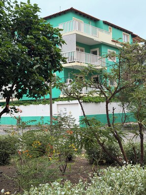 A two-story building with a balcony, surrounded by greenery and flowering plants. - Verd d'Sal Apartment - 200 m from the beach (Santa Maria)