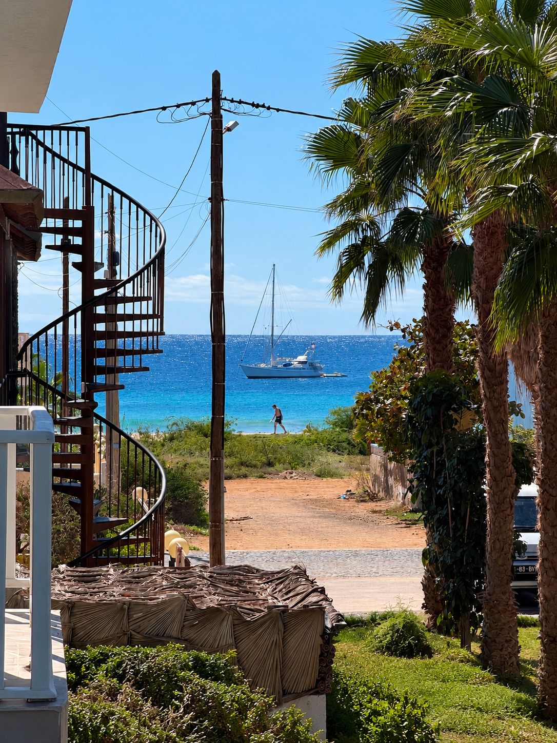 A spiral staircase leading to a balcony overlooking a beach with a sailboat in the distance.