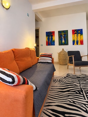 A living room with a sofa, a chair, and a rug. There are paintings on the wall. - Verd d'Sal Apartment - 200 m from the beach (Santa Maria)
