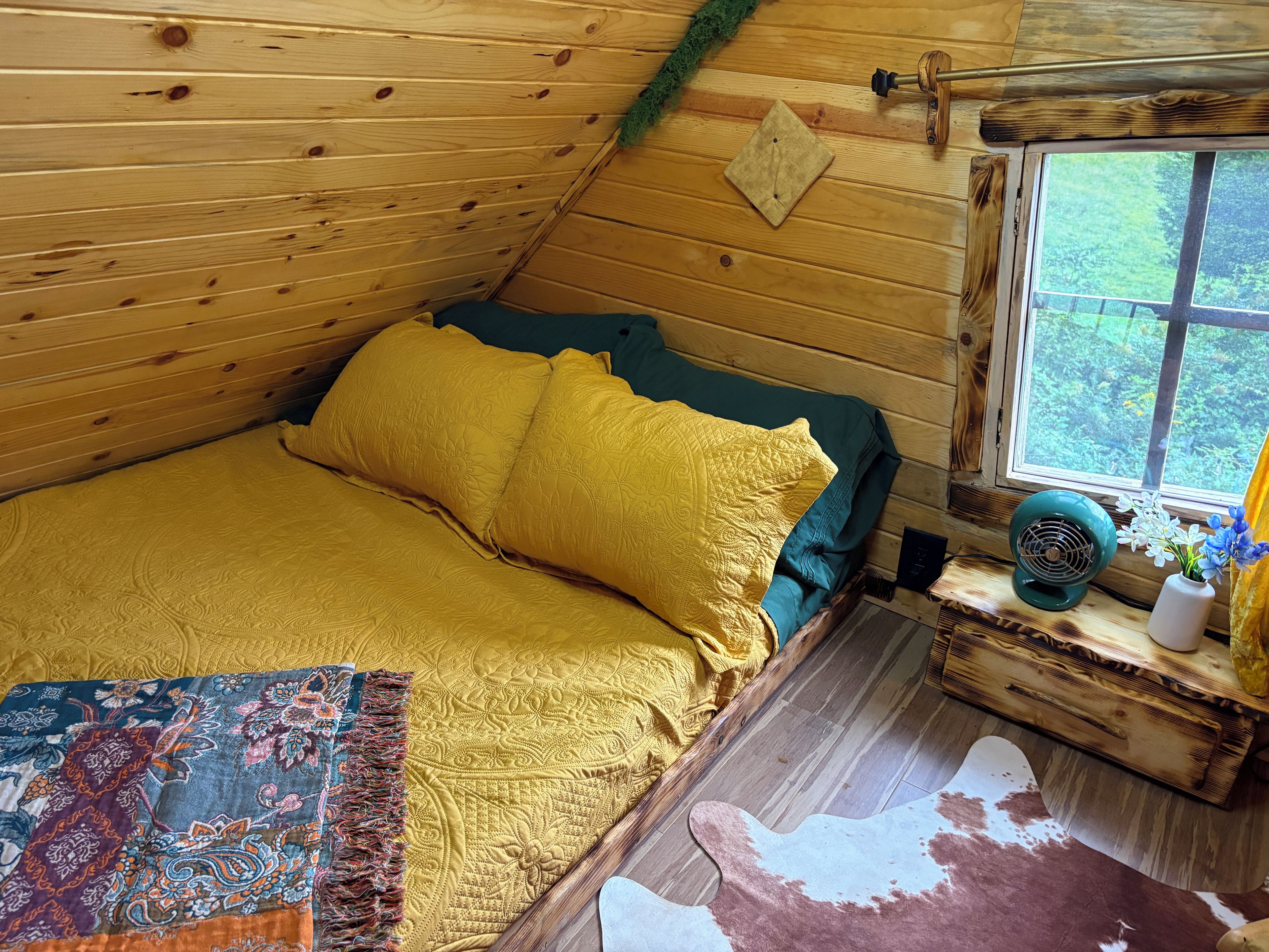 A cozy cabin bedroom with a bed, a window, a fan, and a decorative rug.
