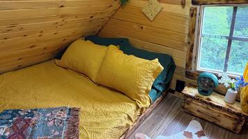 A cozy cabin bedroom with a bed, a window, a fan, and a decorative rug.