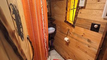 A wooden cabin bathroom with a shower curtain, a toilet, and a window.