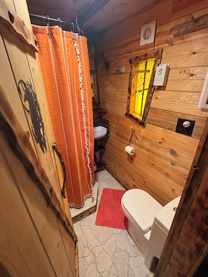 Baño de cabaña de madera con cortina de ducha, inodoro y ventana.