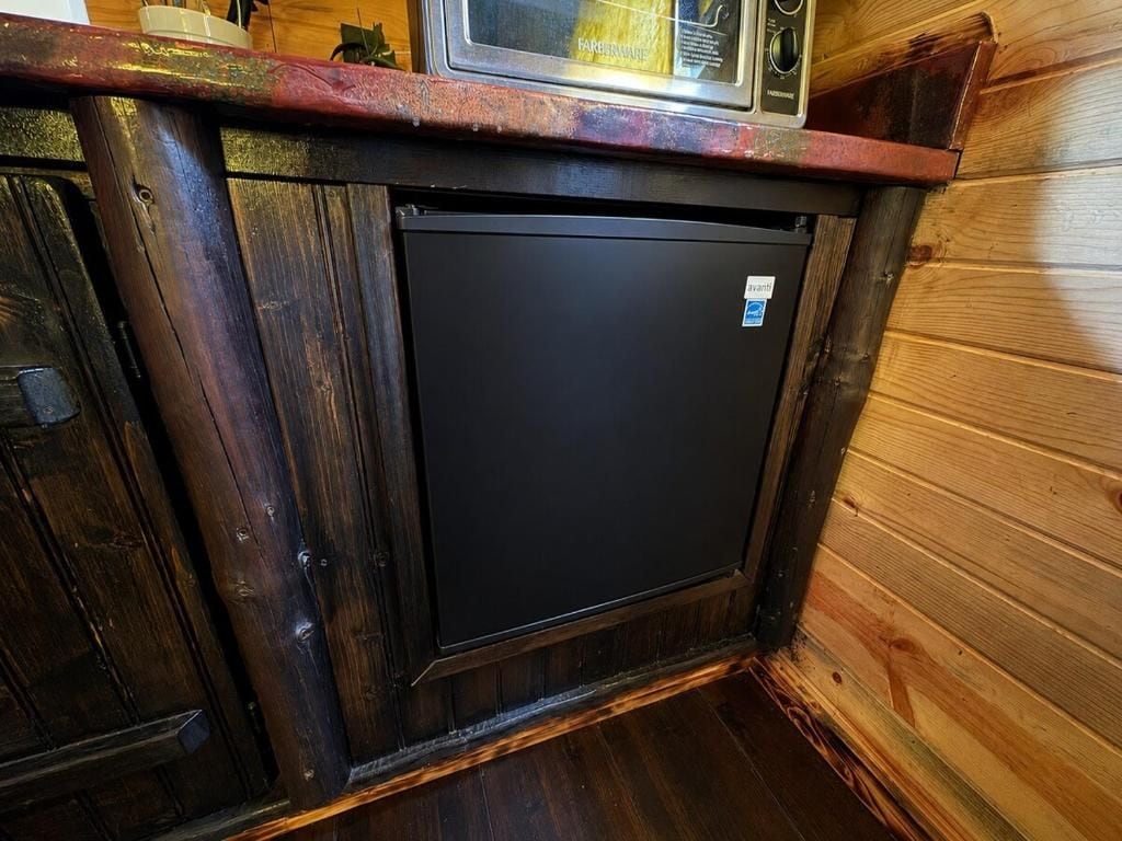 A compact kitchen with a microwave, refrigerator, and wooden cabinetry.