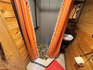 A narrow bathroom with wooden walls, a shower, and a toilet.