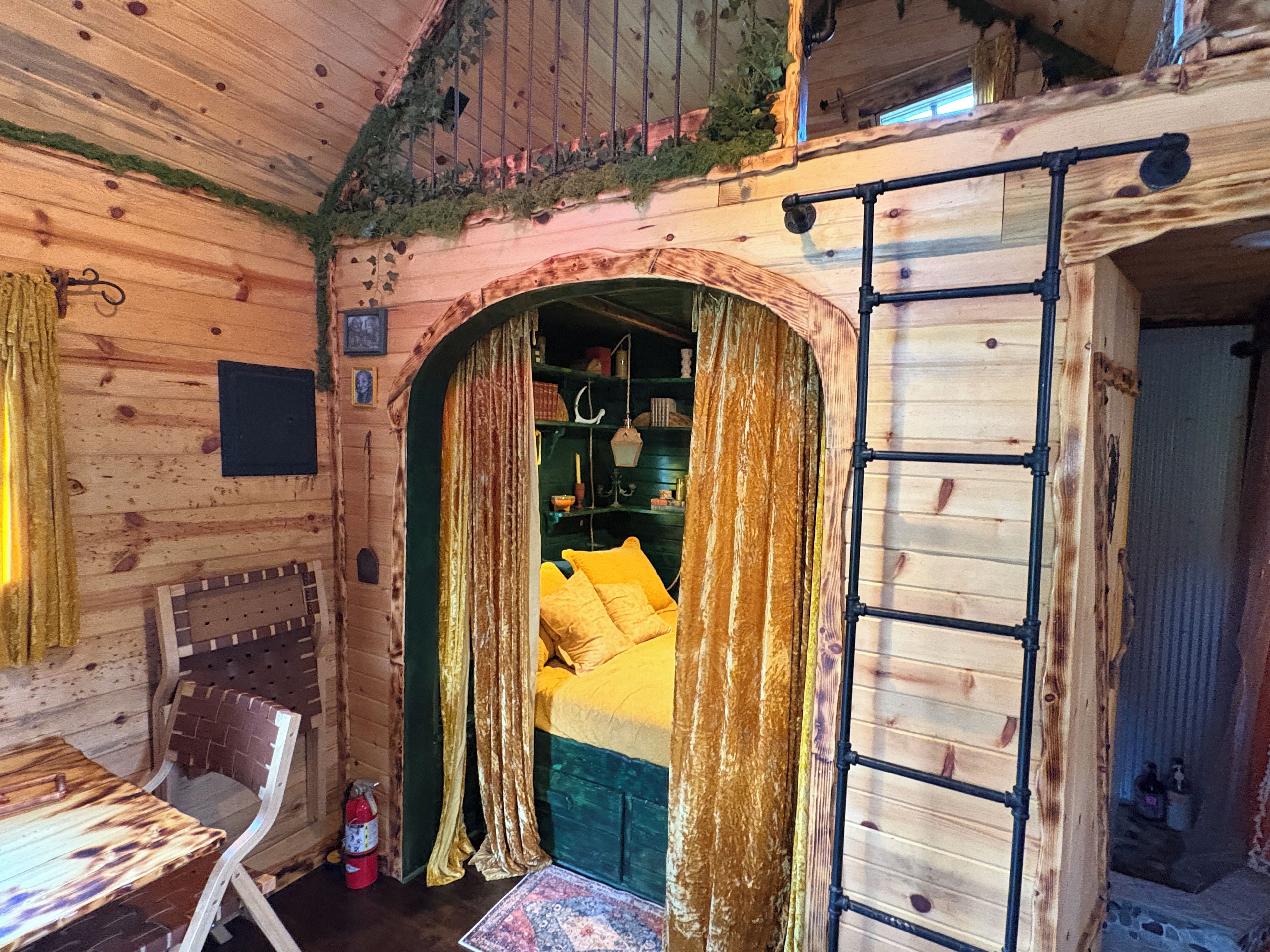 A rustic wooden room with a bed, a chair, a ladder, and a small table.