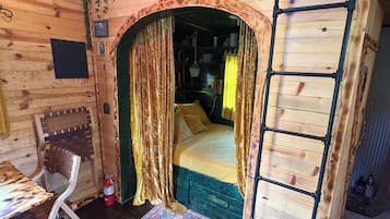 A wooden room with a bed, a ladder, a chair, and a small table.