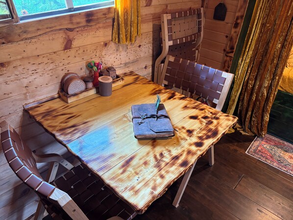 Une table de salle à manger en bois, une chaise à assise tressée, un livre avec une plume et un objet décoratif posé sur la table.