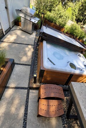 Una vasca idromassaggio con un patio in legno, un barbecue e un vialetto in pietra.