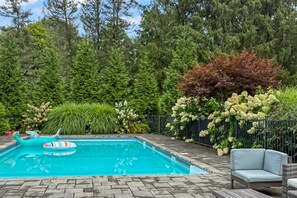 A swimming pool with a tiled deck, surrounded by lush greenery and a variety of plants. - Peaceful Pond House | Sleeps 11, Pool, Wildlife & Room to Gather (Bethlehem)