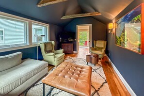 A cozy living room with a sofa, two armchairs, a leather ottoman, a television, and a painting on the wall. - Peaceful Pond House | Sleeps 11, Pool, Wildlife & Room to Gather (Bethlehem)