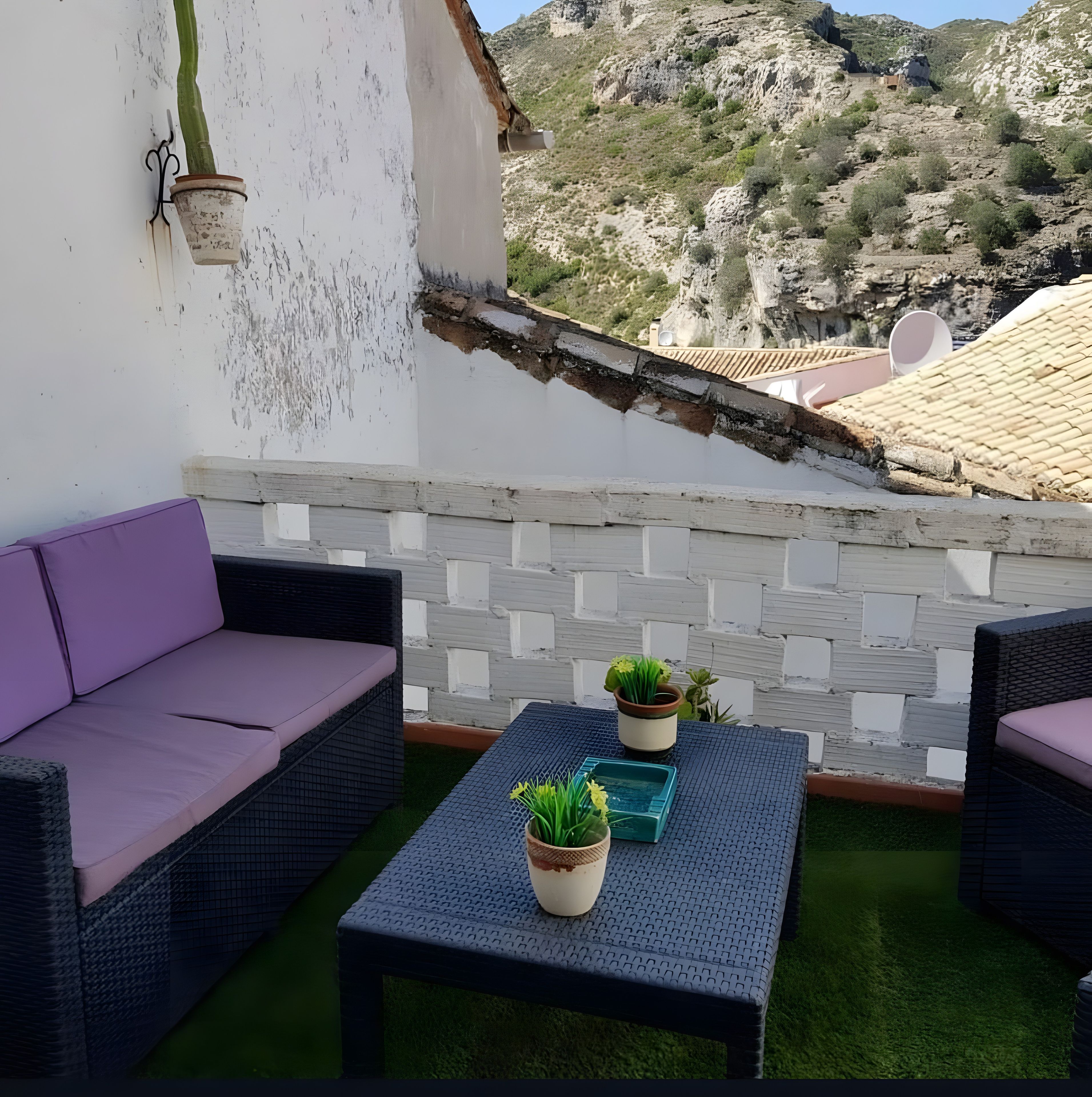 Ein Balkon mit einer Korbuschlaue, einem kleinen Tisch und Blumentöpfen.