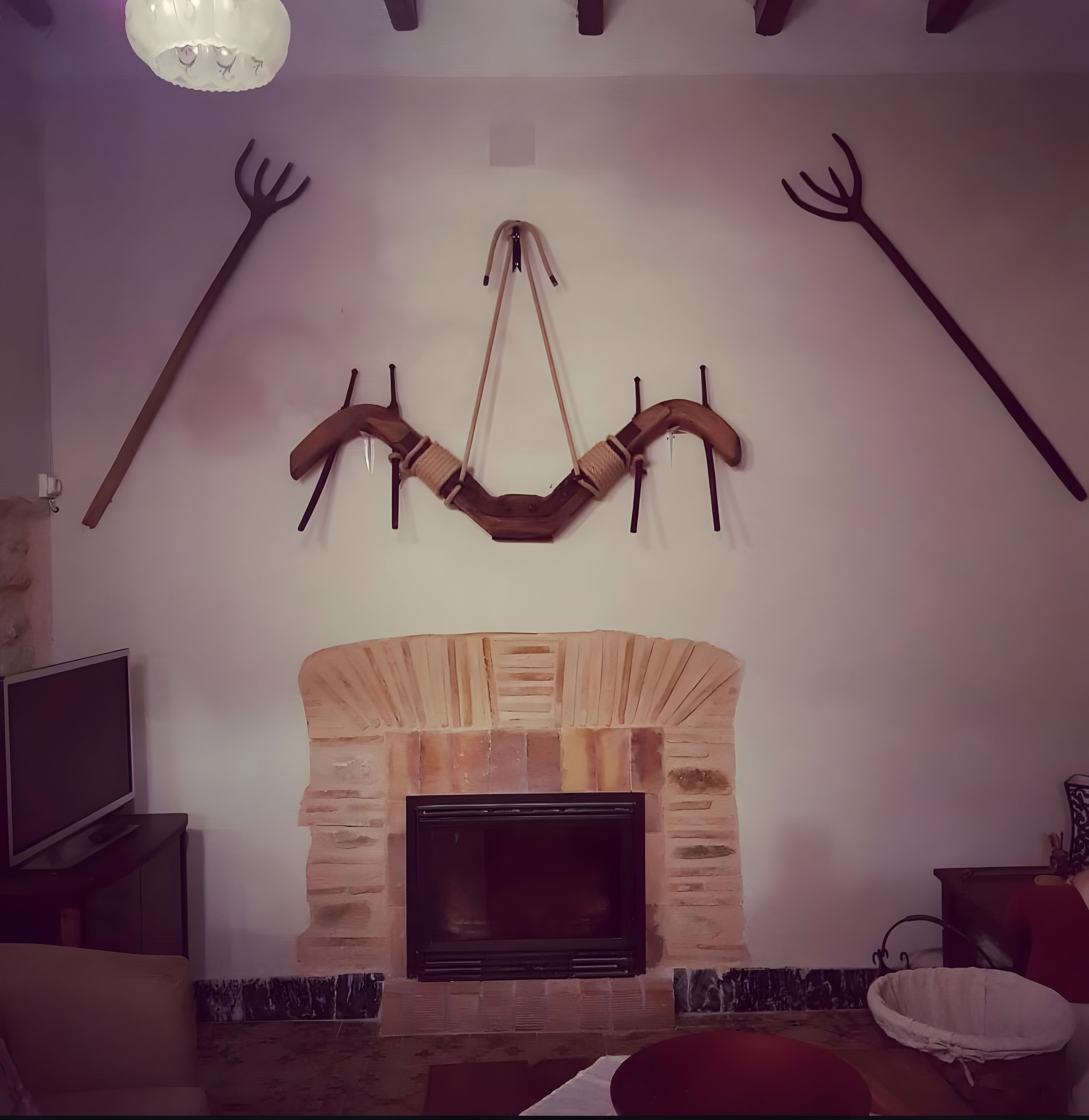 Una sala de estar con chimenea de piedra, un arco de madera montado en la pared y un televisor sobre un mueble.