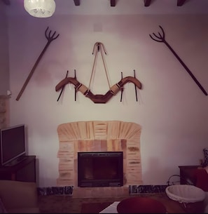 A living room with a stone fireplace, a mounted wooden arch, and a television on a stand.