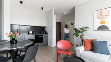 Et moderne køkken med hvide skabe, et spiseområde med et rundt bord og stole, samt en opholdsstue med sofa og hynder.