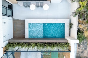 A modern outdoor pool area with a tiled wall, two round tables, and a seating bench. - Studio in Condo. w/ Pool & Sea View One0602 (Salvador)