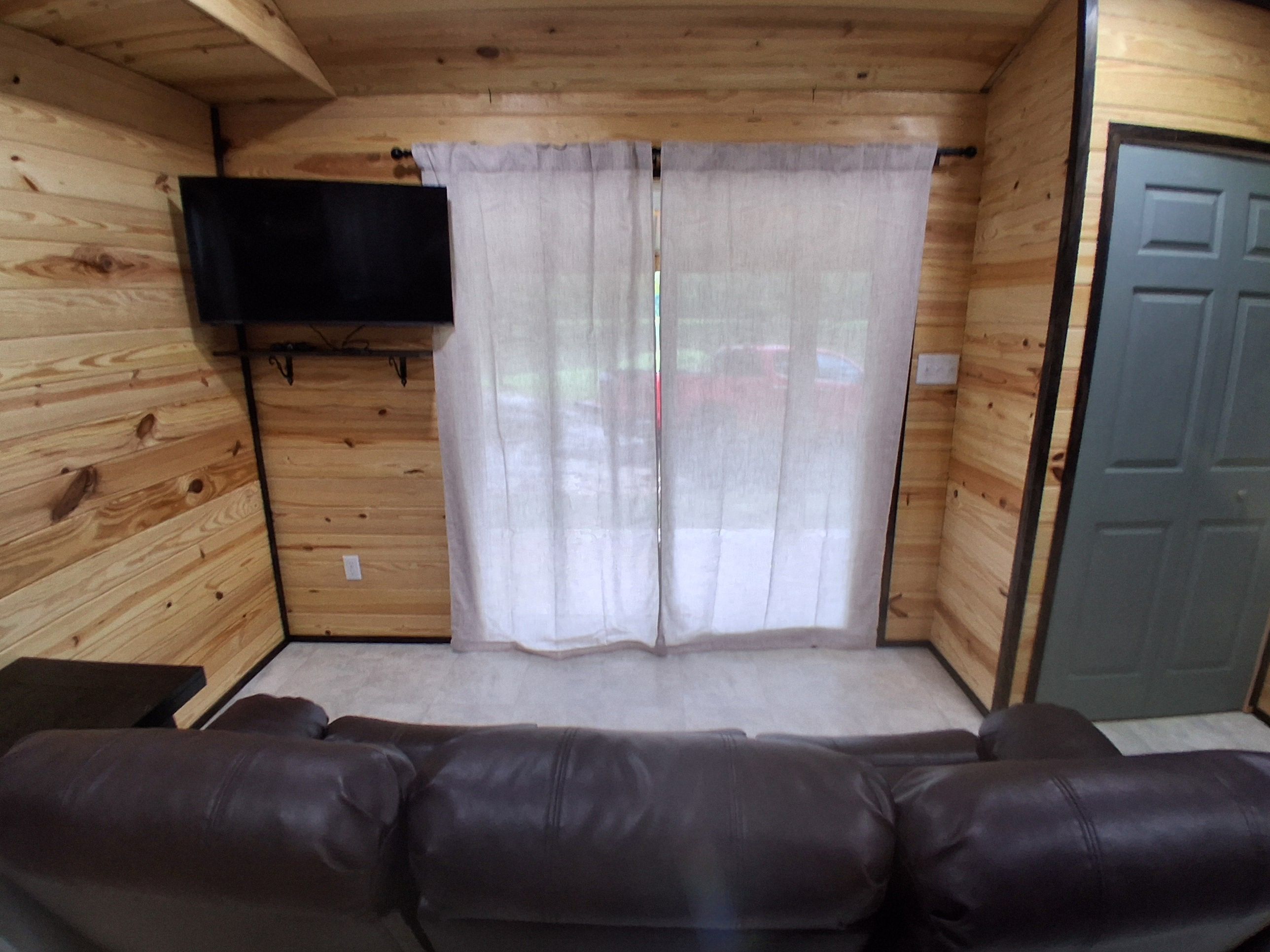 A wooden interior with a sofa, curtains, and a television mounted on the wall.