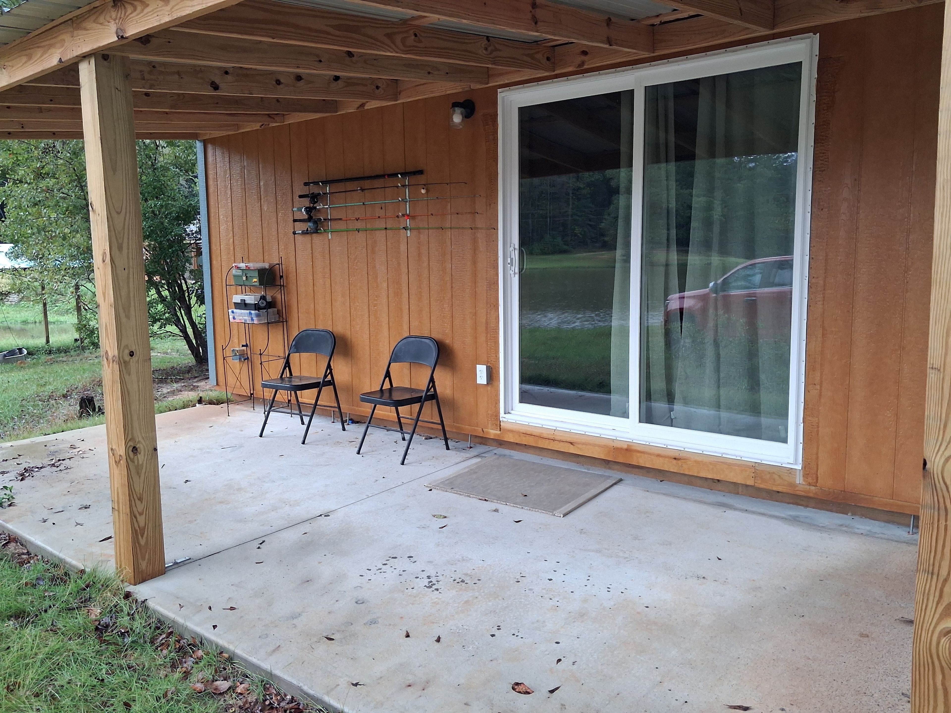 A covered patio area with two chairs, a table, and a sliding glass door leading to a garage.