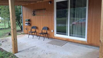 A covered patio area with two chairs, a table, and a sliding glass door leading to a garage.