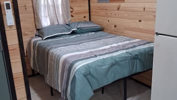 A compact room with a bed, a small white refrigerator, and a wooden wall panel.