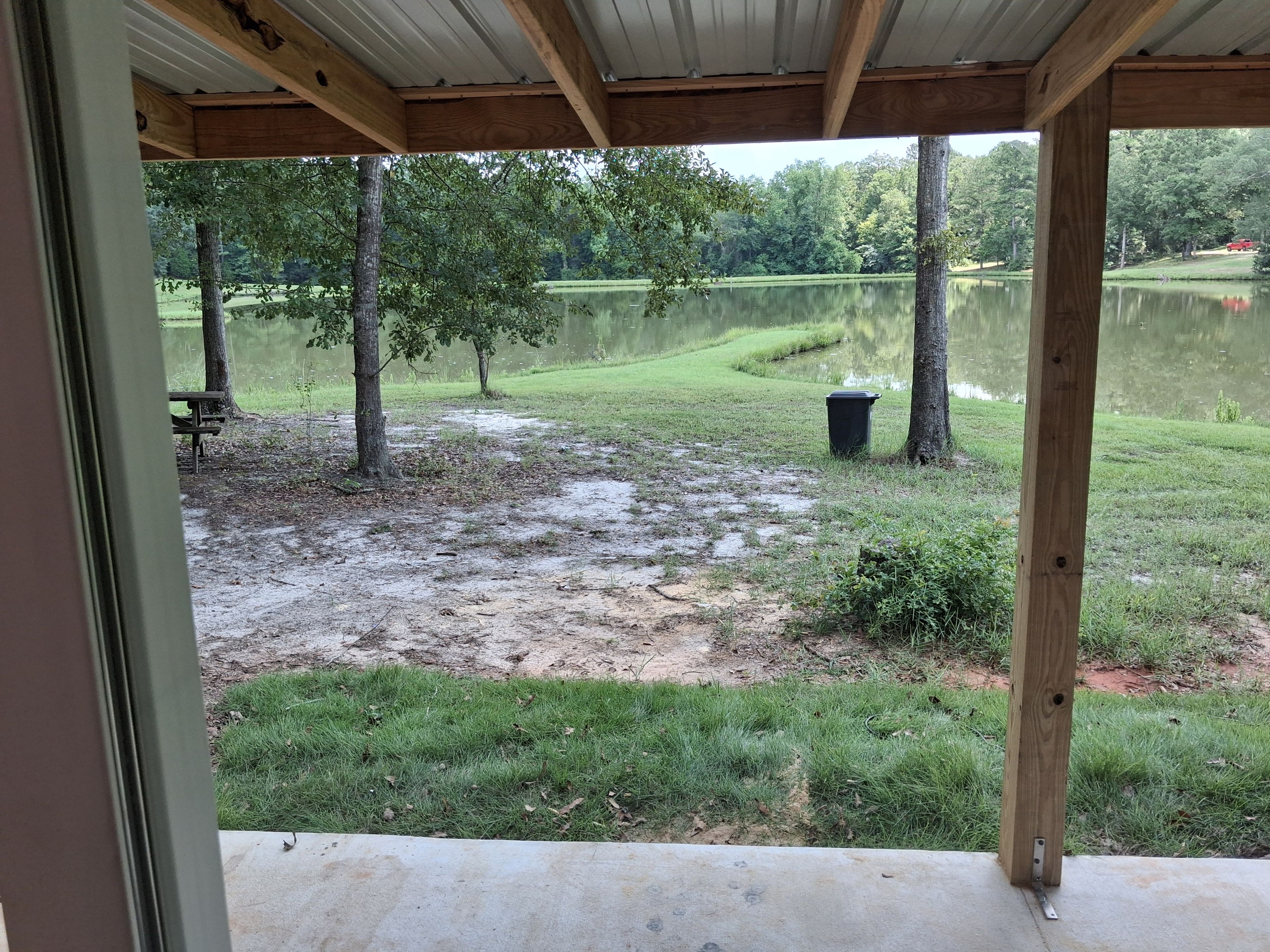 A view from a covered area overlooking a grassy field with trees and a body of water.