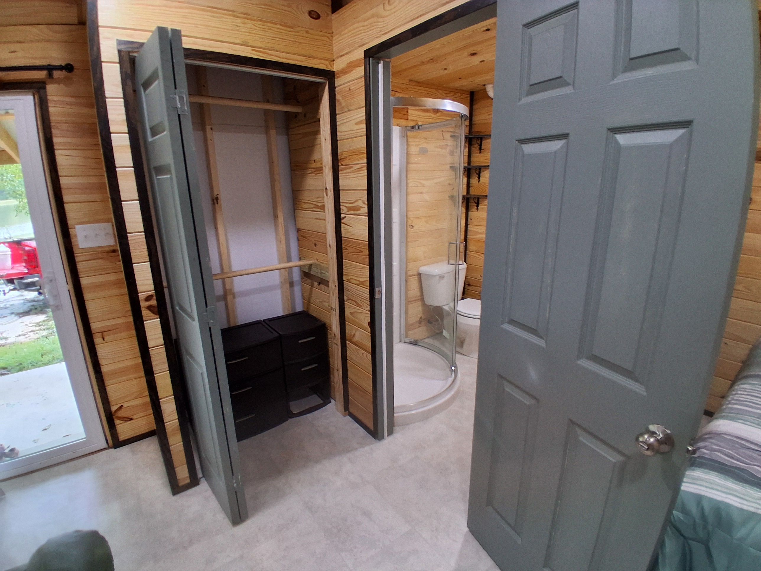 A room with a wooden interior, a grey door, a closet with black storage units, and a toilet.