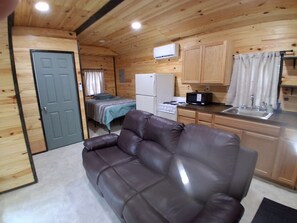 A compact living space with a sofa, a bed, a kitchenette, and a door.