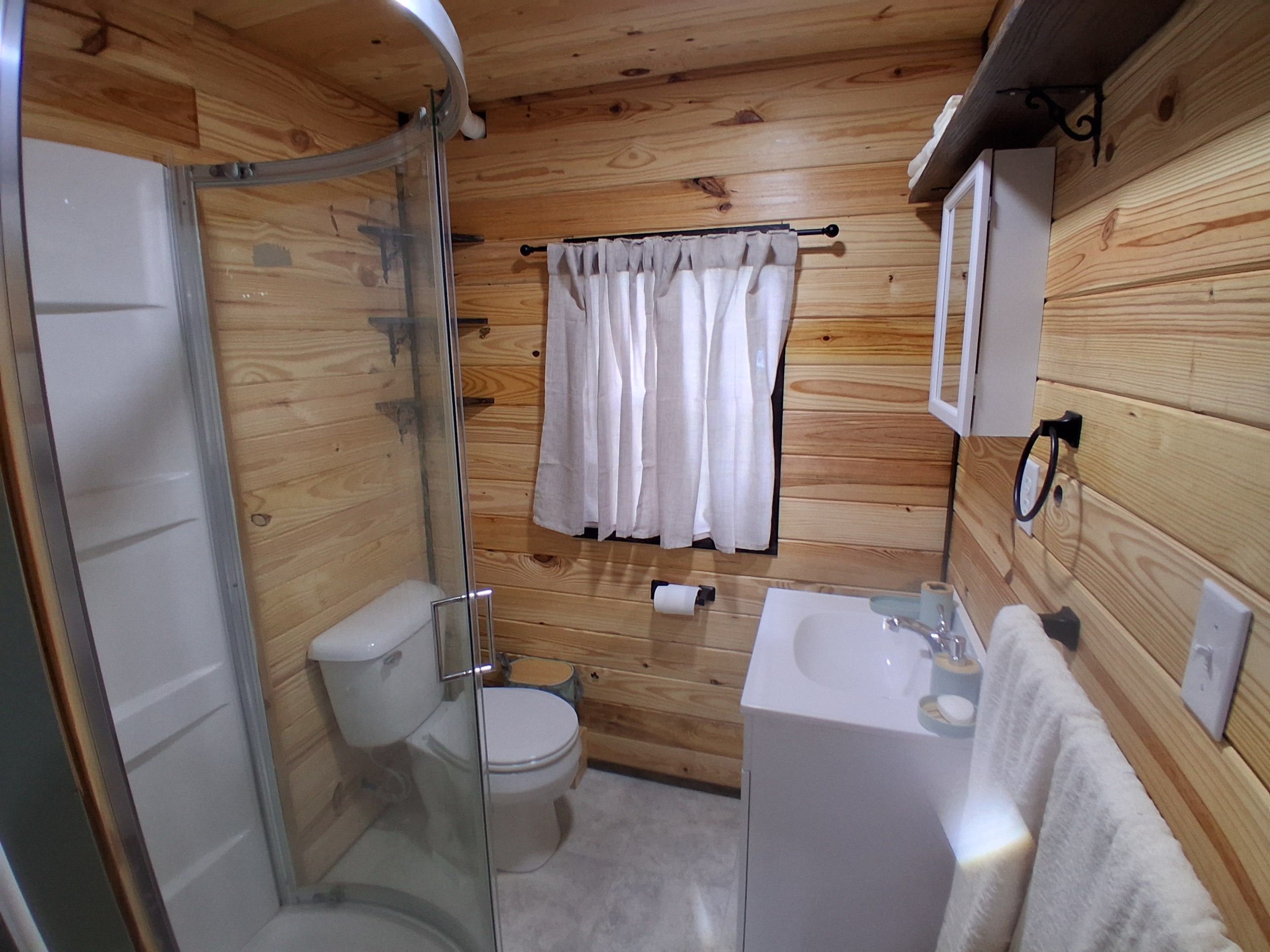 A wooden-paneled bathroom with a glass-enclosed shower, a toilet, a sink, and a towel hanging on a rack.