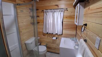 A wooden-paneled bathroom with a glass-enclosed shower, a toilet, a sink, and a towel hanging on a rack.