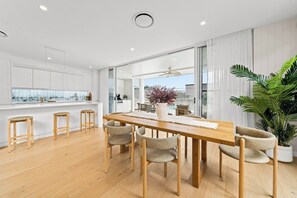 A modern kitchen with a wooden dining table and chairs, a large window, and a view of the outdoors. - West End Luxe Home | Pool & BBQ | Dual living (Brisbane)