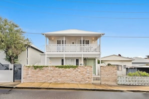 A two-story residential building with a balcony, a brick wall, and a gated entrance. - West End Luxe Home | Pool & BBQ | Dual living (Brisbane)