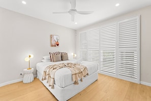A bedroom with a bed, bedside tables, a ceiling fan, and white shutters. - West End Luxe Home | Pool & BBQ | Dual living (Brisbane)
