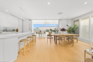 A modern kitchen with a central island, wooden chairs, and a dining area with a view. - West End Luxe Home | Pool & BBQ | Dual living (Brisbane)