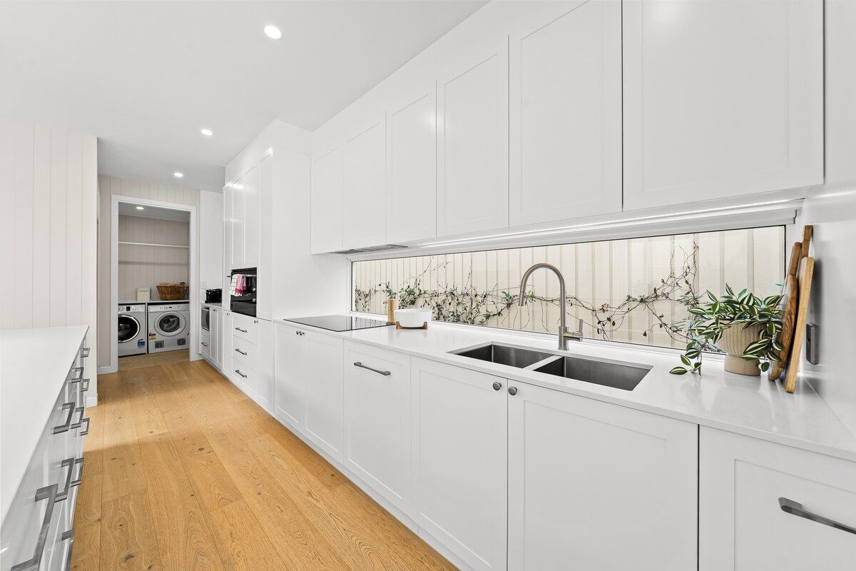 A modern kitchen with white cabinetry, a double sink, and a built-in oven.