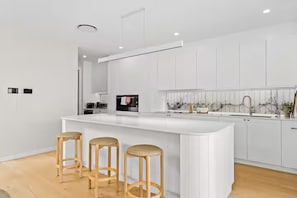 A modern kitchen with a white island, bar stools, and a large window. - West End Luxe Home | Pool & BBQ | Dual living (Brisbane)